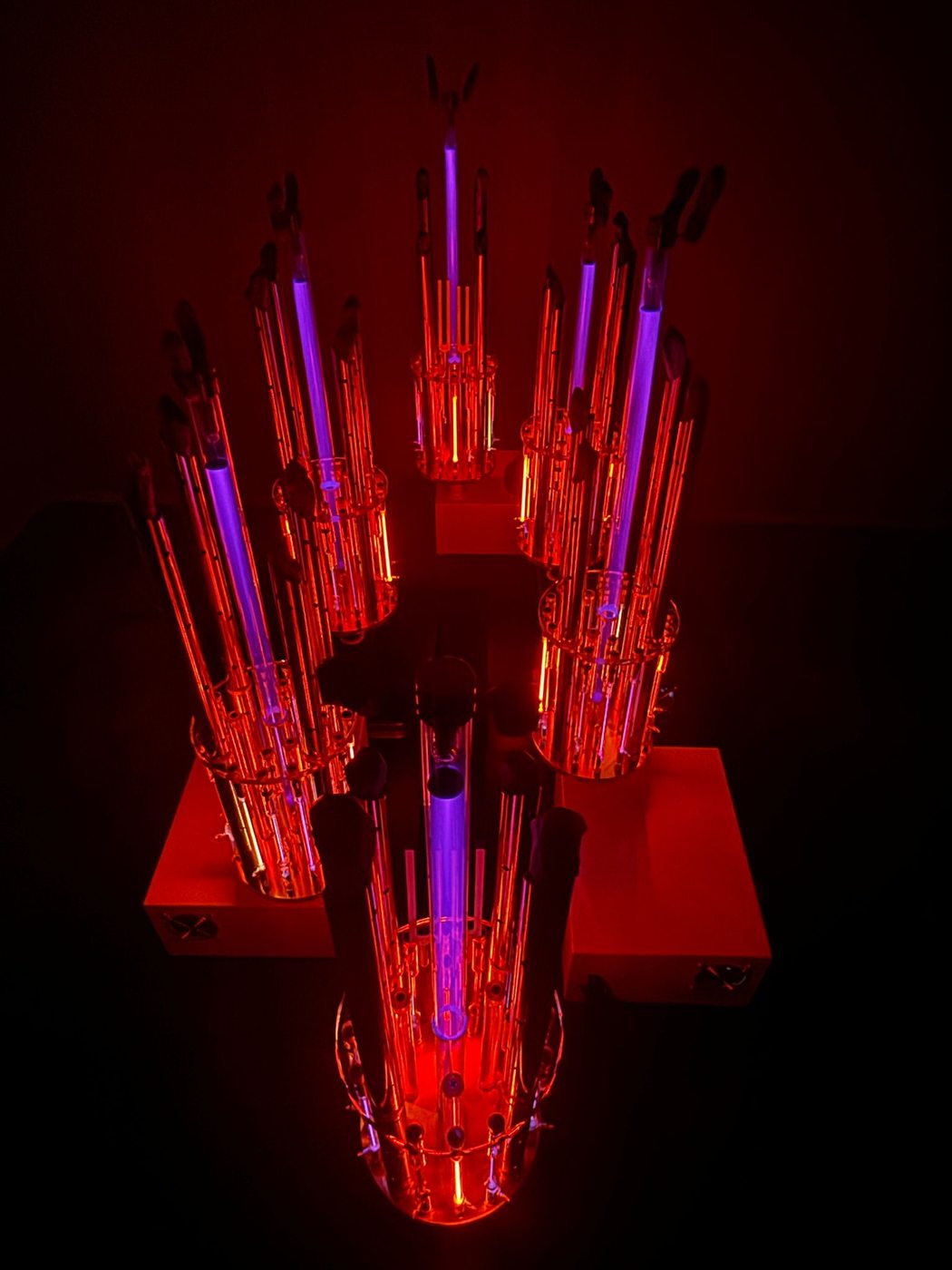 Six Tesla BioLights devices arranged in pyramidal formation, glowing violet and red in a dark practitioner space