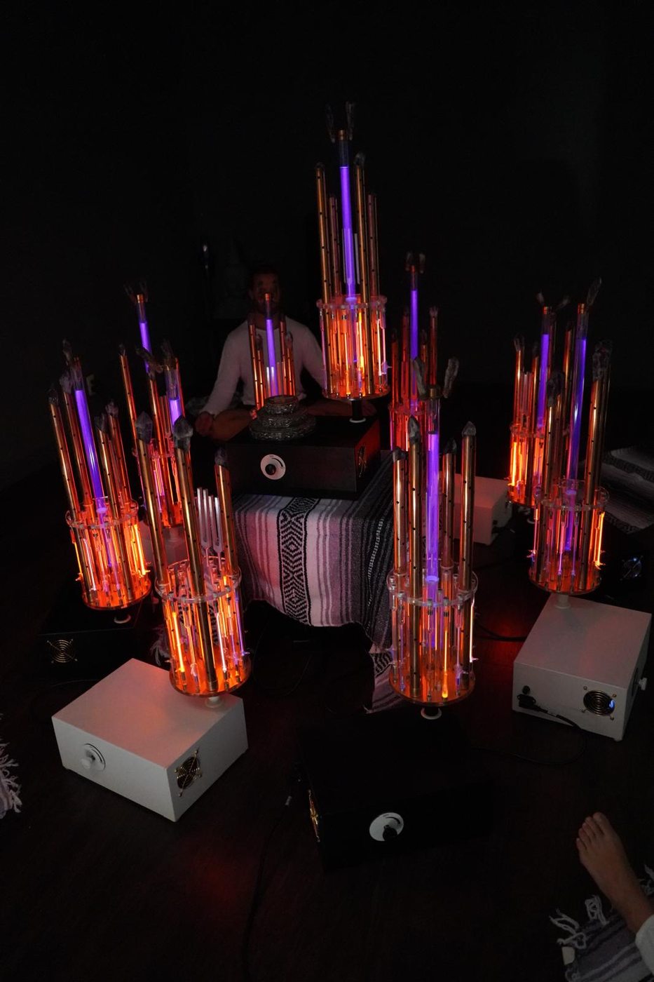 A practitioner in white sitting in meditation inside a ring of seven Tesla BioLights devices glowing red and violet