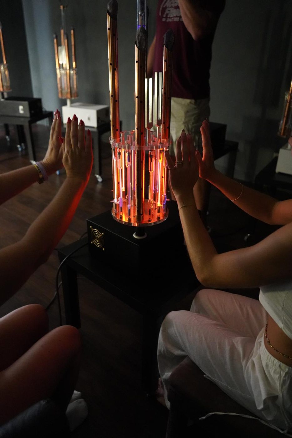 Multiple people's hands extended toward a glowing Tesla BioLights device in a group experience setting