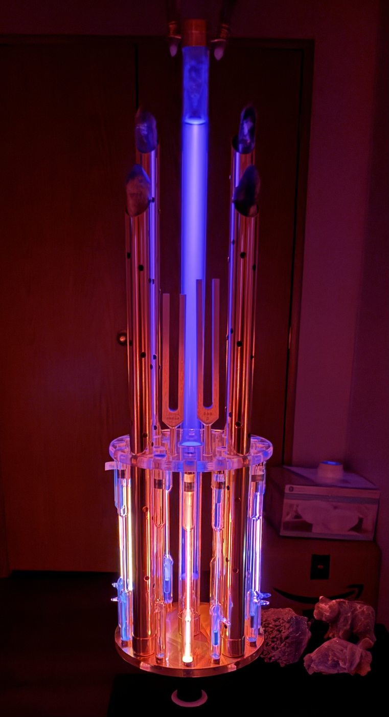 Close-up of a single Tesla BioLights device: bright violet plasma center column, copper coil, amethyst Vogel crystals, in red ambient light